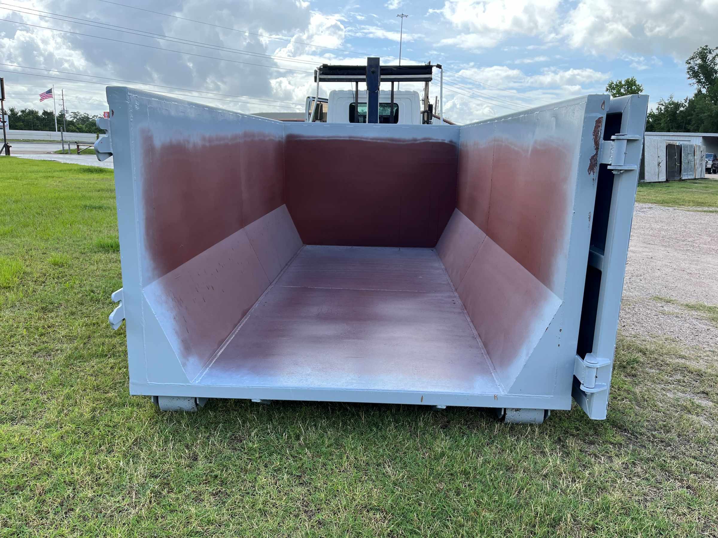 Empty dumpster on a grassy area, showcasing its interior and clean condition. Ideal for waste disposal; situated near a roadside.