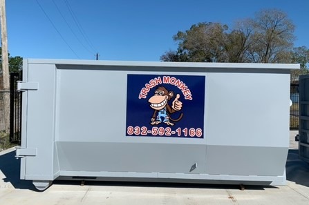 Gray dumpster with a colorful "Trash Monkey" logo, featuring a cartoon monkey, emphasizing waste management services. Contact number included.